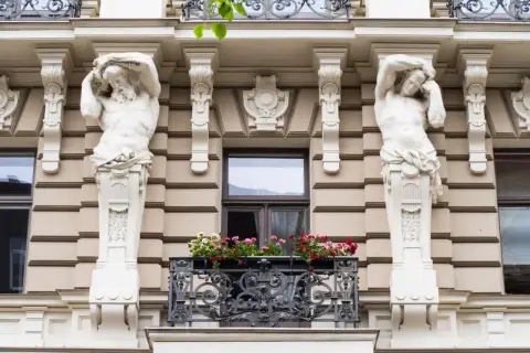 Dwie rzeźby atlantesów podtrzymują balkon z kwiatami. To przykład stylu secesja, co to za sztuka!