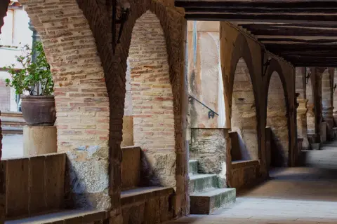 Pasaje abovedado de piedra y ladrillo con arcos, bancos de piedra y una planta en maceta. Un lugar con encanto para pasear y descubrir la fresneda que ver.