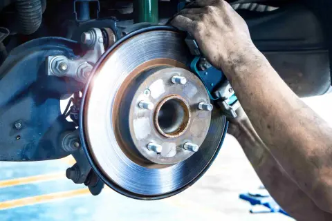 Mécanicien remplaçant la garniture de frein usure d'une Mercedes. Le disque de frein est visible, ainsi que les mains sales du technicien.