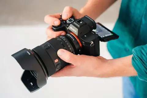 Dłonie trzymają aparat Sony a7r5 z obiektywem.
