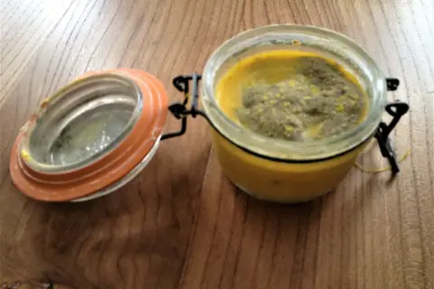 Terrine le parfait recette : un pot en verre avec un couvercle orange ouvert, contenant une préparation jaune et verte sur une table en bois.