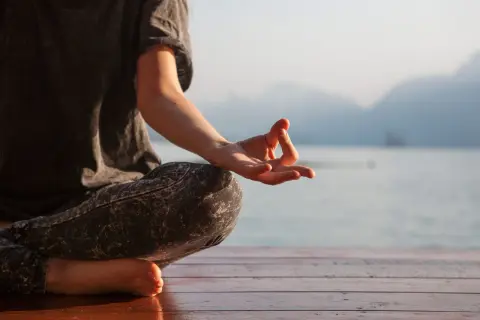 Persona meditando en posición de loto, con la mano en mudra Gyan, susurrando el mantra om.