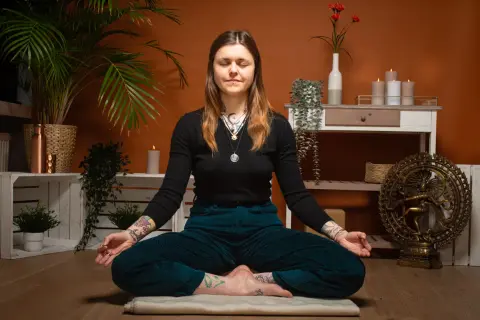 Frau in tiefer meta meditation, umgeben von Pflanzen und Kerzen. Eine Shiva-Statue im Hintergrund.