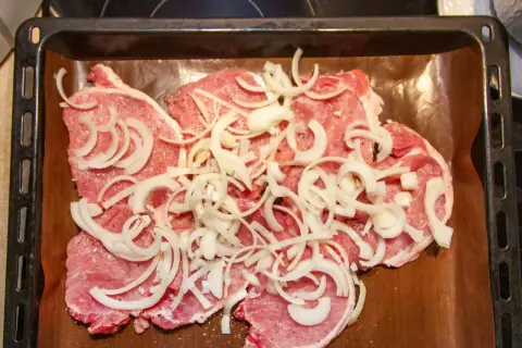 Plastry schabu pieczonego w cebulce, przyprawione i ułożone na blasze wyłożonej papierem do pieczenia.