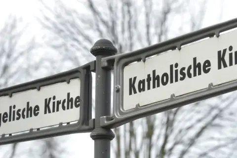 Straßenschilder zeigen "Evangelische Kirche" und "Katholische Kirche". Ein deutlicher Unterschied katholisch evangelisch, der die Vielfalt der Glaubensrichtungen symbolisiert.