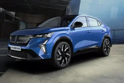 Une voiture hybride non rechargeable bleue, au design moderne, se gare devant un bâtiment aux lignes architecturales audacieuses.