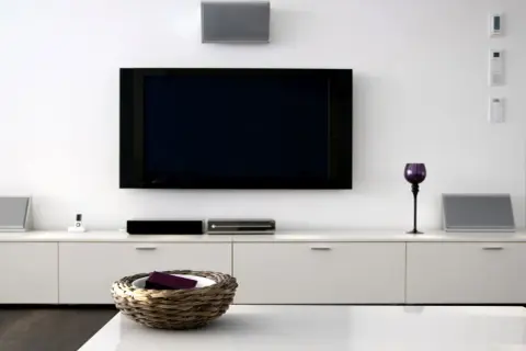 Nowoczesny salon z dużym telewizorem na ścianie, białymi meblami i dekoracjami.