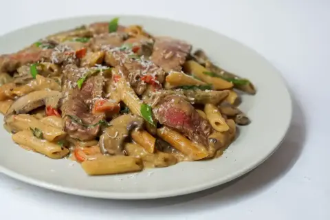 Penne z kawałkami soczystej wołowiny w kremowym sosie z pieczarkami i pomidorkami. Idealne, co w piątek na obiad zamiast ryby.
