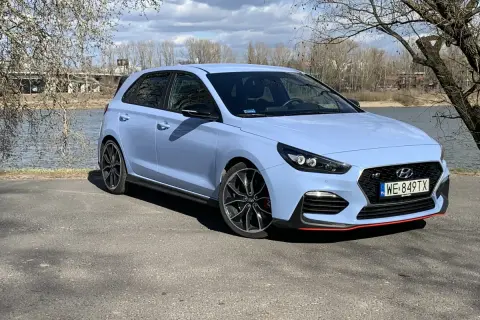 Niebieski Hyundai i30 N z czerwonymi akcentami stoi nad jeziorem, gotowy na wiosenną przejażdżkę.