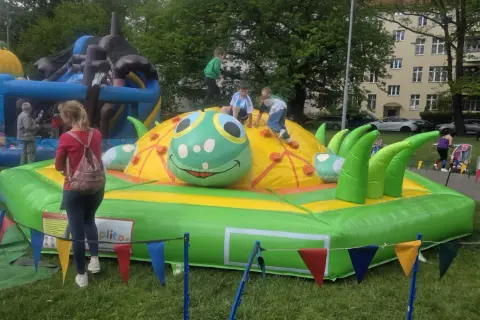 Dzieci bawią się na dmuchanej gąsienicy, która jest jedną z atrakcji dla 3 latka. W tle widać inne dmuchańce i budynek mieszkalny.
