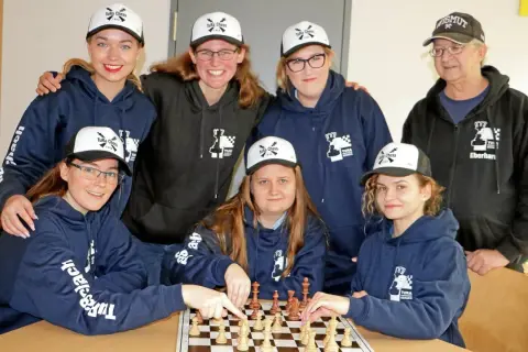 Grupa osób w bluzach i czapkach z logo "TuRa Chess" gra w szachy.