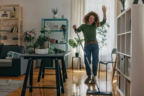 Donna sorridente lava il pavimento con uno straccio, un esempio di come tenere in ordine la casa con gioia.