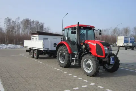 Czerwony traktor z przyczepą, gotowy do egzaminu na prawo jazdy na traktor. Litera "L" na zderzaku.