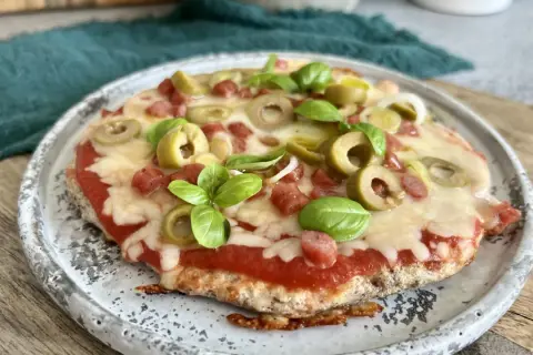 Mini pizza z serka wiejskiego, z sosem pomidorowym, oliwkami, kiełbaską i bazylią, na talerzu.