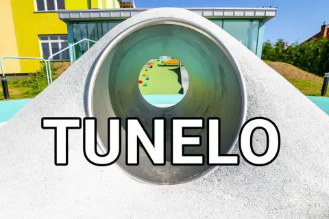 Tunel na placu zabaw z widokiem na kolorowe elementy i budynek.