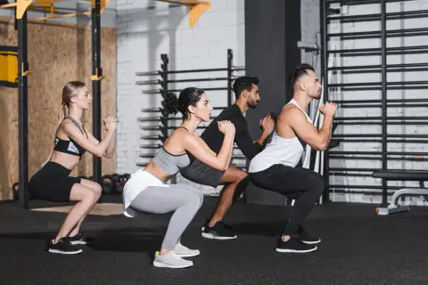 Uomini e donne eseguono squat a corpo libero in palestra, concentrati sull'esercizio.
