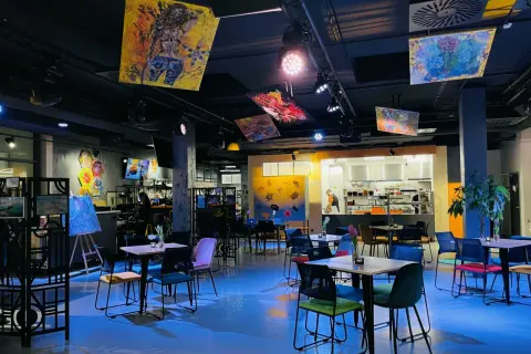 Wnętrze Oria Magic House z kolorowymi obrazami na suficie i ścianach. Stoliki i krzesła tworzą przytulną atmosferę, idealną do przeglądania menu.