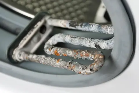 Stark verkalkter Heizstab einer Waschmaschine. Kalkablagerungen beeinträchtigen die Leistung und Lebensdauer. Zeit, die Waschmaschine zu entkalken!