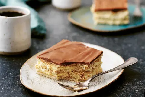 En bit chokladkaka med mariekex och krämig fyllning, perfekt för ett mariekex recept. En kopp kaffe står bredvid.