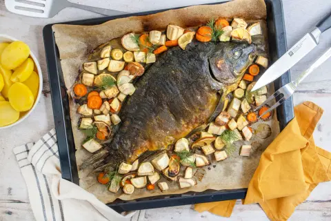 Schuppenkarpfen zubereiten: Ganzer Fisch mit Wurzelgemüse und Zitrone auf einem Blech gebacken. Daneben gekochte Kartoffeln.
