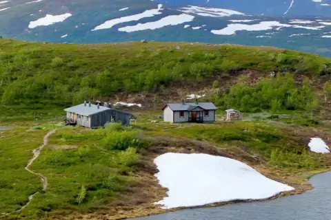 Fjällstugor vid en sjö, med snöfläckar kvar på sluttningarna. En idyllisk vy från Saltoluokta mot Kvikkjokk.