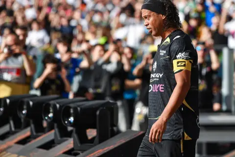 Ronaldinho w czarnej koszulce z żółtym opaską na ramieniu, z tłumem w tle.