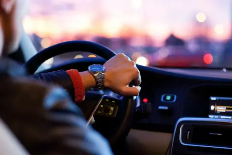 Förare med klocka styr bil med automatlåda genom stadens ljus i skymningen.
