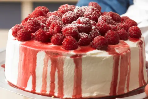Himbeer Joghurt Torte, üppig belegt mit frischen Himbeeren und Puderzucker, mit roten Himbeersaucen-Tropfen.