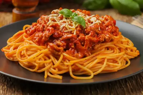 Pyszne spaghetti bolognese, idealne na prosty obiad. Makaron z bogatym sosem mięsnym, posypany serem i udekorowany bazylią.