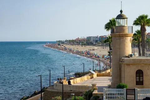 Faro de Roquetas de Mar, Almería, con una playa abarrotada de gente disfrutando del sol y el mar.