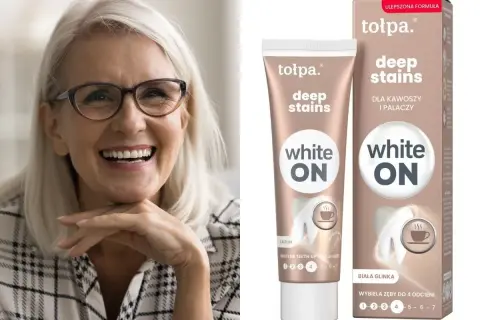 Uśmiechnięta kobieta z jasnymi włosami i okularami. Obok tubka i pudełko pasty do zębów Tołpa Deep Stains White ON – jaka pasta wybielająca dla kawoszy i palaczy.