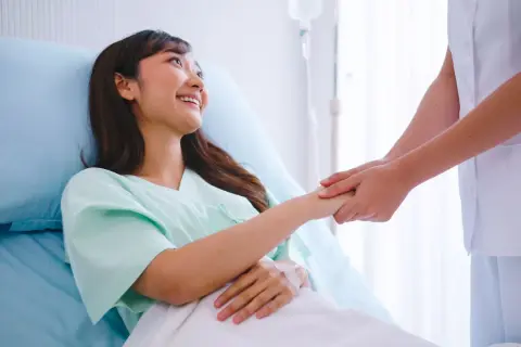 Una paciente sonríe mientras una enfermera le toma la mano, ofreciendo apoyo tras las contracciones después del parto.