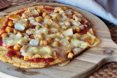 Pizza sin queso con garbanzos y trozos de queso derretido sobre una base crujiente.