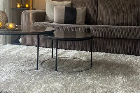 Gemütliches Wohnzimmer mit einem Sofa in greige Farbe, zwei Marmor-Couchtischen und einem flauschigen Teppich.