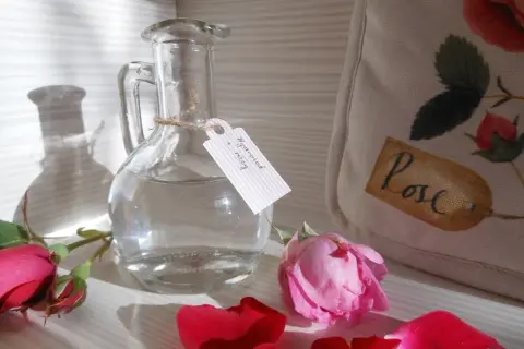 Szklana butelka z etykietą "Hydrolat z róży" i płatkami róż. Idealny sposób, jak zrobić hydrolat w domu.