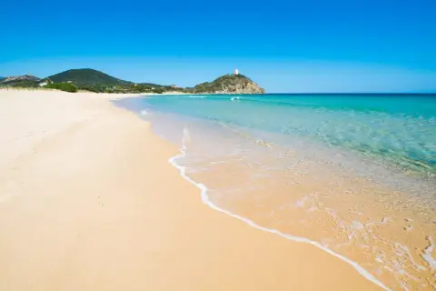 Piękne plaże Cagliari, z turkusową wodą i złotym piaskiem, zapraszają do relaksu. W oddali widać wieżę na wzgórzu.