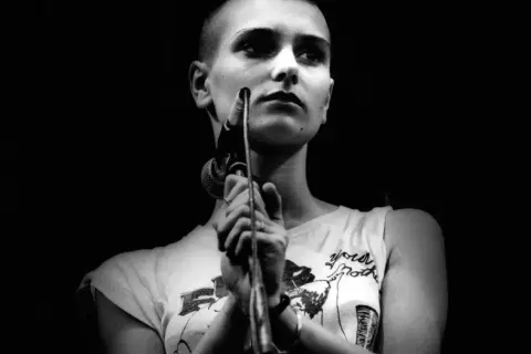 Sinéad O'Connor śpiewa "Nothing Compares 2 U", jej twarz jest oświetlona, a ona trzyma mikrofon.
