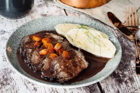 Klassisches Sauerbraten Rezept im Backofen: Zartes Rindfleisch in dunkler Soße mit Karotten und Klößen, garniert mit Dill.