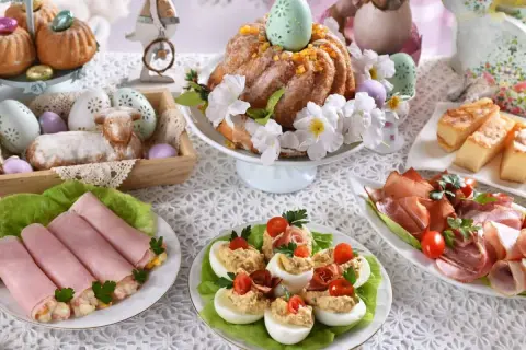 Udekorowany stół na śniadanie wielkanocne: babka, baranek, jajka faszerowane, wędliny i ciasto.