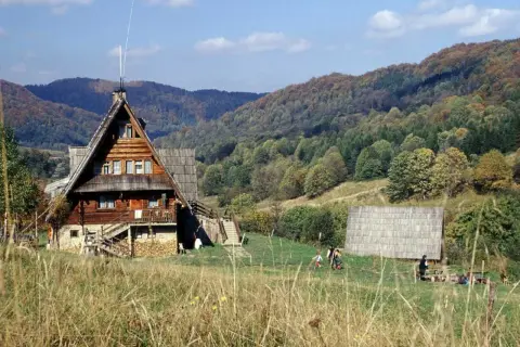 Drewniane schroniska górskie w Polsce, otoczone jesiennymi lasami. Ludzie odpoczywają na trawie, ciesząc się widokiem.