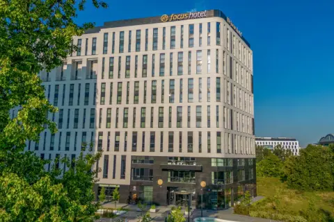 Nowoczesny budynek Focus Hotel Premium Warszawa z zielenią i błękitnym niebem. Idealne miejsce na pobyt.