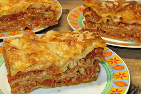Prosty przepis na lasagne z mięsem mielonym. Pyszne, warstwowe danie z makaronem, sosem mięsnym i serem, podane na kolorowych talerzach.