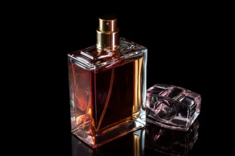 Elegancki flakonik baccarat perfume o bursztynowym kolorze, obok niego mniejszy, przezroczysty korek.