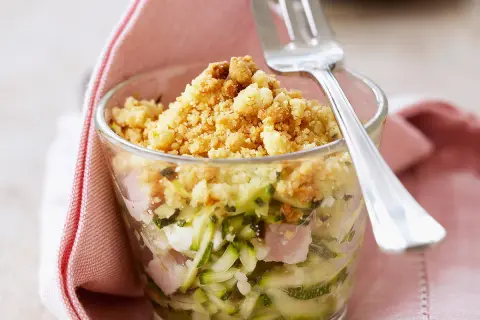 Un délicieux crumble de courgettes, jambon et fromage, servi dans un verre, prêt à être dégusté avec une fourchette.