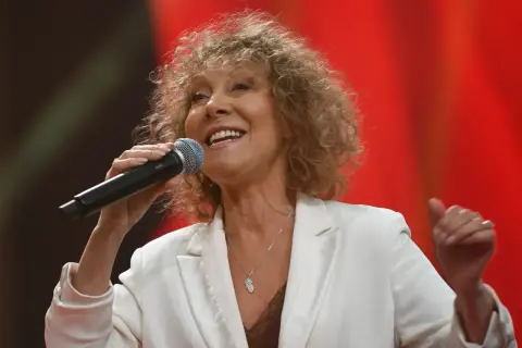 Alicja Majewska, mimo swojego wieku, wciąż zachwyca na scenie. Uśmiechnięta, z mikrofonem w dłoni, w białej marynarce.