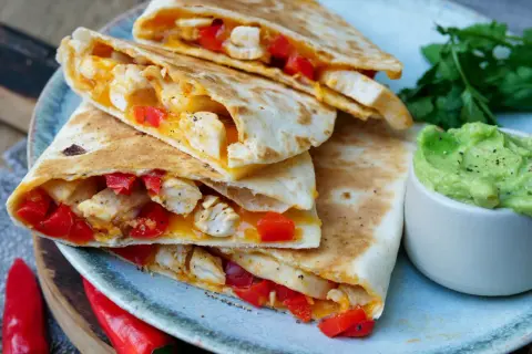 Leckeres Quesadillas Rezept: goldbraune Tortillas gefüllt mit Hähnchen, roter Paprika und geschmolzenem Käse, serviert mit Guacamole.