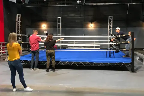 A group discusses a 12 week boxing training program around a wrestling ring.