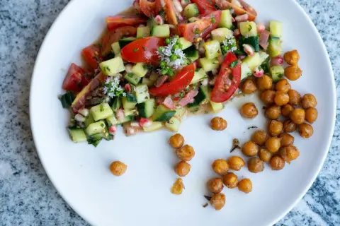 Salade colorée de tomates, concombres et pois chiches rôtis, garnie de petites fleurs blanches.