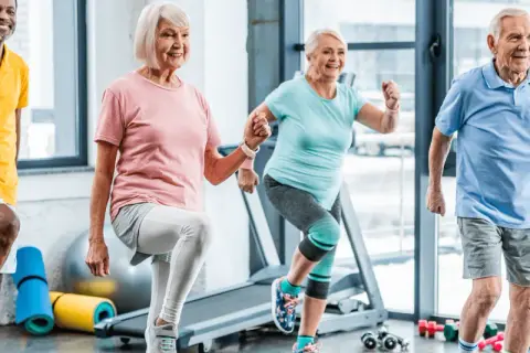 Quatre seniors souriants font de l'exercice ensemble. Voici 5 arguments pour le sport : vitalité, joie, santé, longévité et bien-être.