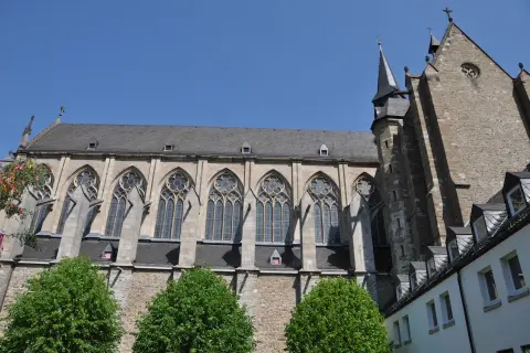 Der Altenberger Dom ragt mit seinen gotischen Fenstern und steinernen Mauern in den blauen Himmel. Grüne Bäume säumen das imposante Bauwerk.